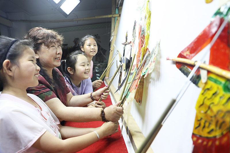 皮影藝人指導(dǎo)小朋友表演皮影戲。